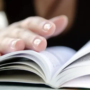 Hands holding a book open on a desk.