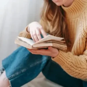 Woman in tan sweater reading a book.