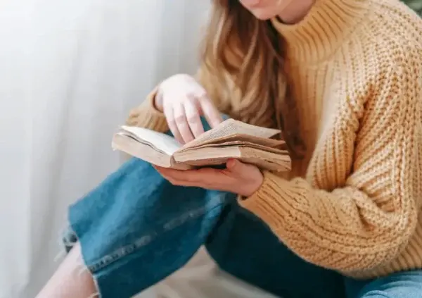 Woman in tan sweater reading a book.