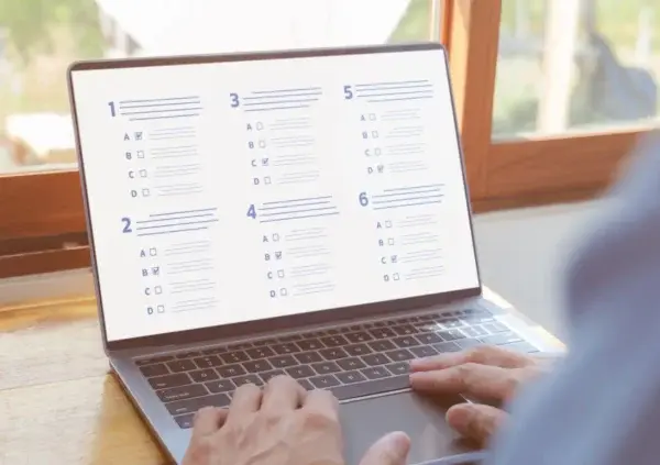 Man taking an multiple choice assessment on a laptop by a window.
