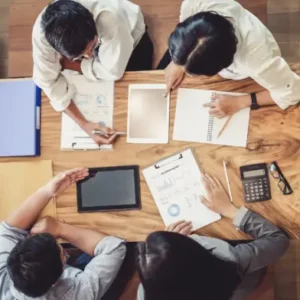 Team of professionals working on a busy desk with tablets, reports, and a calculator.